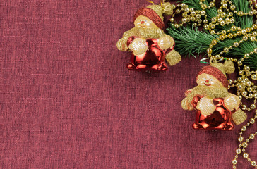 Background in the form of Christmas decorations and toy snowmen under the spruce branch on a burgundy fabric surface on the right, on the left - an empty space