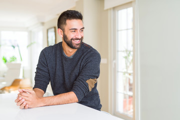 Fototapeta na wymiar Handsome hispanic man wearing casual sweater at home looking away to side with smile on face, natural expression. Laughing confident.