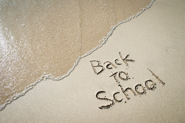Fototapeta premium Back to School message handwritten on smooth sand beach with incoming wave
