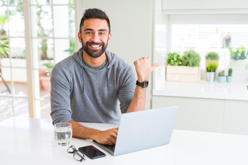 Handsome hispanic man working using computer laptop pointing and showing with thumb up to the side with happy face smiling