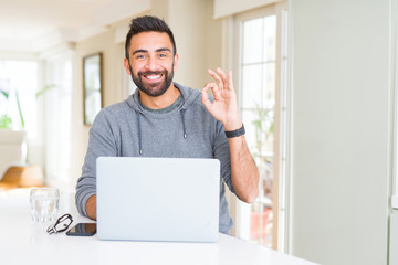 Handsome hispanic man working using computer laptop doing ok sign with fingers, excellent symbol