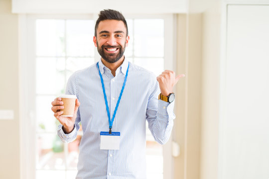 Handsome hispanic man wearing id card and drinking a cup of coffee pointing and showing with thumb up to the side with happy face smiling