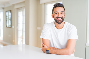 Handsome hispanic man casual white t-shirt at home happy face smiling with crossed arms looking at the camera. Positive person.