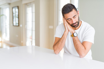 Handsome hispanic man casual white t-shirt at home sleeping tired dreaming and posing with hands together while smiling with closed eyes.