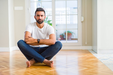 Fototapeta na wymiar Handsome hispanic man wearing casual t-shirt sitting on the floor at home skeptic and nervous, disapproving expression on face with crossed arms. Negative person.