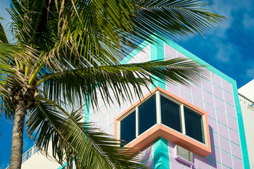 Corner detail of brightly colored Art Deco architecture in pastel pink and blue with tropical palm tree in Miami, Florida, USA