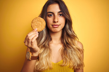 Young beautiful woman eating biscuit over grey isolated background with a confident expression on...