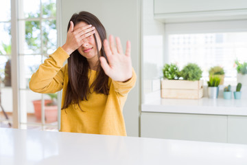 Beautiful young woman wearing yellow sweater covering eyes with hands and doing stop gesture with...