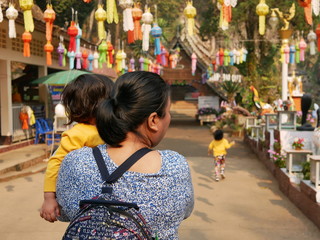 Asian woman carrying and taking her little baby girl to visit a Buddhist temple - travel helps ignite children's imagination and encourages them to embrace their new experiences during their childhood