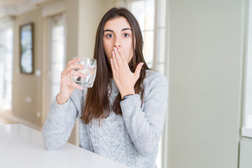 Beautiful young woman drinking a fresh glass of water cover mouth with hand shocked with shame for mistake, expression of fear, scared in silence, secret concept