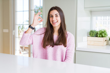 Beautiful young woman wearing pink sweater smiling positive doing ok sign with hand and fingers. Successful expression.