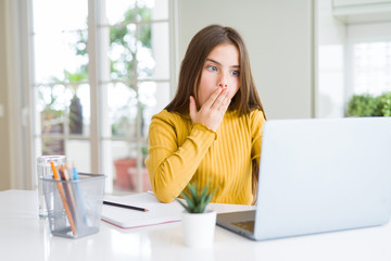 Beautiful young girl studying for school using computer laptop cover mouth with hand shocked with...
