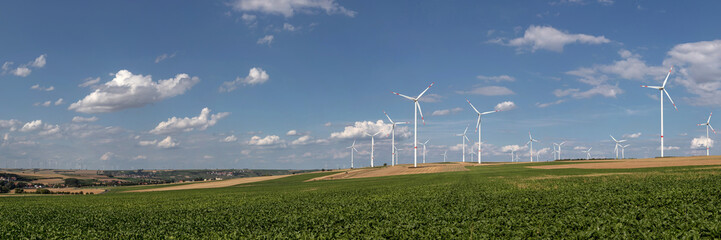 Panoramic view of Wind turbines on the fields under a blue sky with some clouds © kraichgaufoto