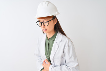 Young chinese engineer woman wearing coat helmet glasses over isolated white background with hand on stomach because nausea, painful disease feeling unwell. Ache concept.