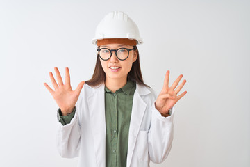 Young chinese engineer woman wearing coat helmet glasses over isolated white background showing and pointing up with fingers number nine while smiling confident and happy.