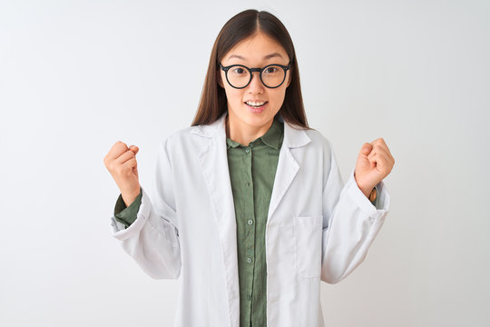 Young chinese scientist woman wearing coat and glasses over isolated white background celebrating surprised and amazed for success with arms raised and open eyes. Winner concept.