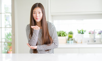 Beautiful Asian woman wearing stripes sweater looking at the camera blowing a kiss with hand on air being lovely and sexy. Love expression.