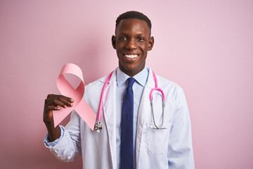 African american doctor man holding cancer ribbon standing over isolated pink background with a...
