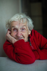 Old lady woman in her house, a portrait sitting at a table in a red jacket.