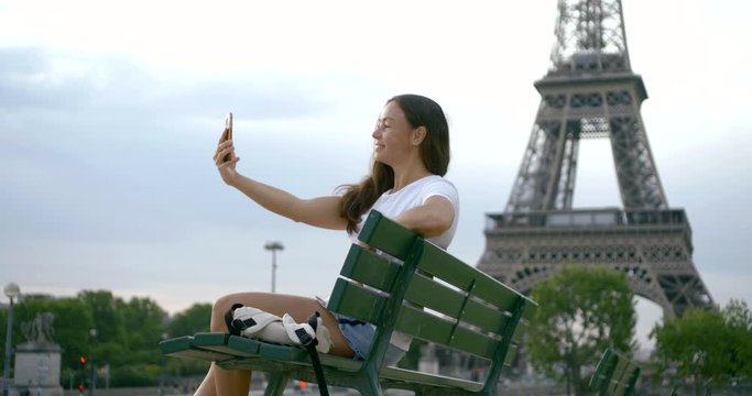 happy woman is sitting on bench in Paris and taking selfie with Eiffel tower