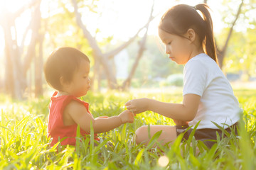 Beautiful young asian kid sitting playing in summer in the park with enjoy and cheerful on green...