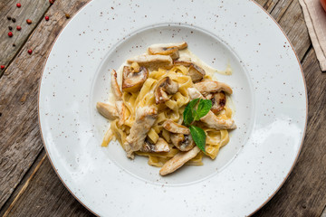 Pasta with chicken and mushrooms on old wooden table