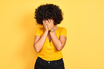 Fototapeta na wymiar Young arab woman with curly hair wearing t-shirt standing over isolated yellow background with sad expression covering face with hands while crying. Depression concept.
