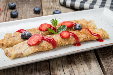 Pancakes with berries and mint on wooden background