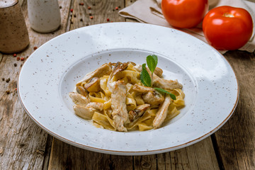 Pasta with chicken and mushrooms on wooden table