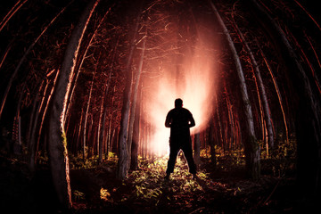strange light in a dark forest at night. Silhouette of person standing in the dark forest with...