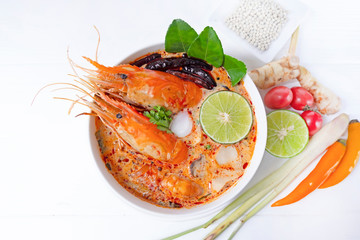 Tom Yum Goong or Shrimp soup spicy sour Soup Traditional food in Thailand contains chili, lime, ginger, galangal, lemongrass, lime leaf, from top view on a white wood background  from top view.