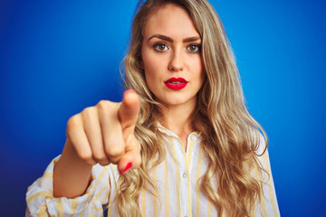 Young beautiful woman wearing striped shirt standing over blue isolated background pointing with finger to the camera and to you, hand sign, positive and confident gesture from the front