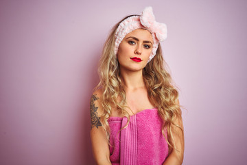 Young beautiful woman wearing towel after shower over pink isolated background with serious expression on face. Simple and natural looking at the camera.