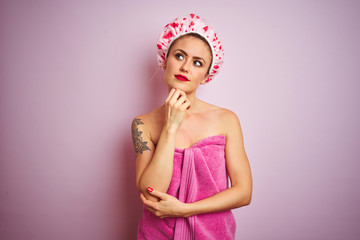 Obraz na płótnie Canvas Young beautiful woman wearing towel and bath hat after shower over pink isolated background with hand on chin thinking about question, pensive expression. Smiling with thoughtful face. Doubt concept.