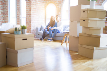 Fototapeta premium Beautiful young asian couple relaxing together sitting on the sofa arround cardboard boxes, happy moving to a new house