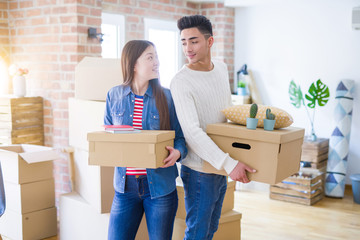 Beautiful young asian couple looking happy holding cardboard boxes, smiling excited moving to a new home