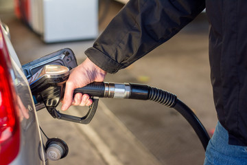 A man in a blue jeans and black coat holding pump filling gasoline. Pumping petrol into the tank. A...