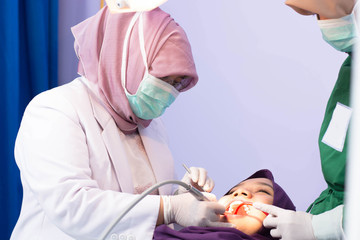 Obraz na płótnie Canvas Musliam Hijab Asian female get her teeth polishing with female dentiist who helping by her assistant in dentist chair on clinic hospital room