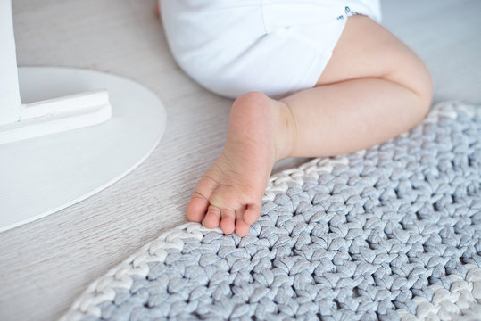 Cute baby in blue overalls sits on a knitted carpet
