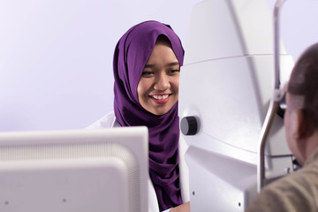 smiling female Muslim Hijab ophthalmologists doing eye examination to her male patient with tonometer and Slit Lamp on the eye clinic