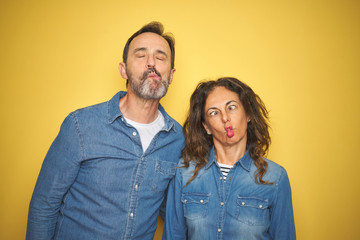 Beautiful middle age couple together standing over isolated yellow background making fish face with lips, crazy and comical gesture. Funny expression.