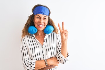 Middle age tourist woman wearing neckpillow and sleep mask over isolated white background smiling with happy face winking at the camera doing victory sign. Number two.