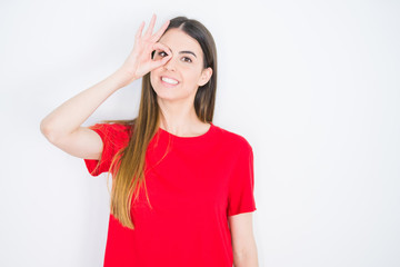 Obraz na płótnie Canvas Young beautiful woman wearing casual red t-shirt over white isolated background doing ok gesture with hand smiling, eye looking through fingers with happy face.