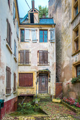 Fototapeta na wymiar Charming crooked little old house with blue roof in cobblestone alley between two buildings