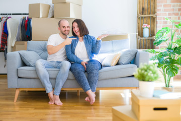 Fototapeta na wymiar Young couple sitting on the sofa arround cardboard boxes moving to a new house amazed and smiling to the camera while presenting with hand and pointing with finger.
