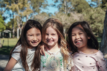 Happy and healthy multiethnic young little girls hugging and smiling in the park, best friends and...