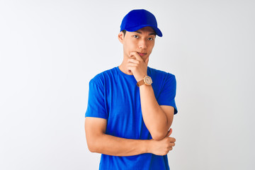Chinese deliveryman wearing blue t-shirt and cap standing over isolated white background looking confident at the camera with smile with crossed arms and hand raised on chin. Thinking positive.