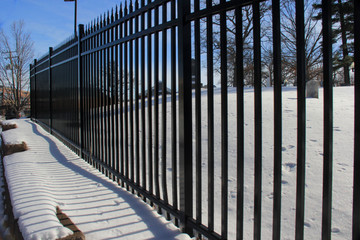 Snow covered ledge, framed by a black rod iron fence, and blue sky.