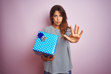 Young beautiful woman holding birthday gift over pink isolated background with open hand doing stop...
