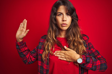 Young beautiful woman wearing casual jacket standing over red isolated background peeking in shock covering face and eyes with hand, looking through fingers with embarrassed expression.